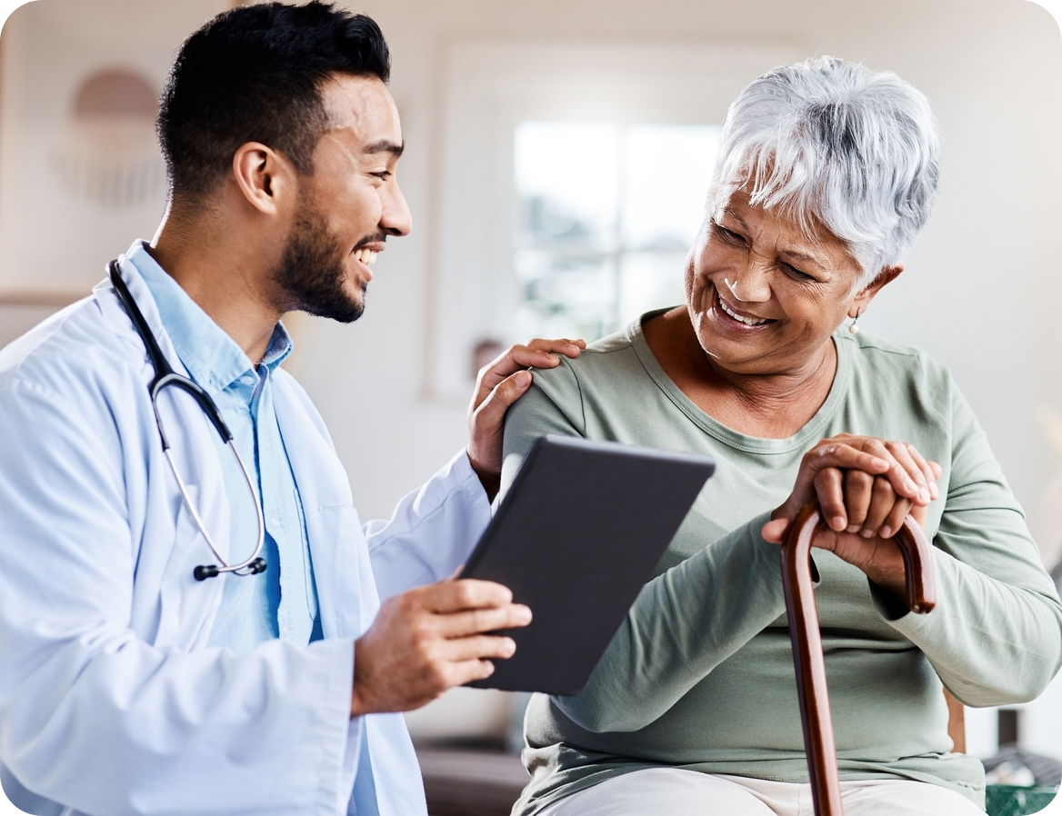 A doctor is holding a tablet computer, with one hand on the shoulder of an elderly patient. They are both smiling while looking at the test results.