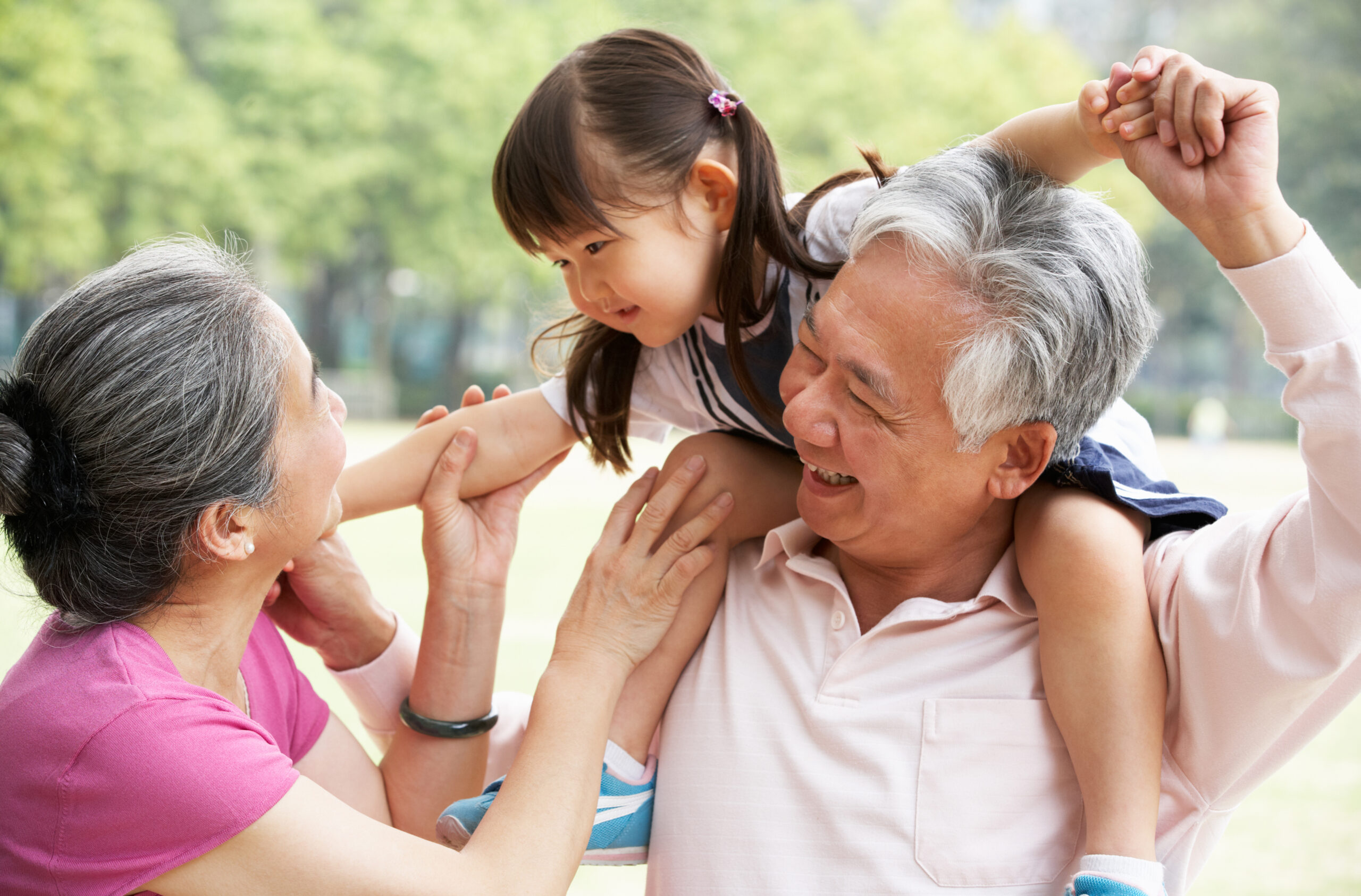 Chinese Grandparents Giving Granddaughter Ride On Shoulders Smiling