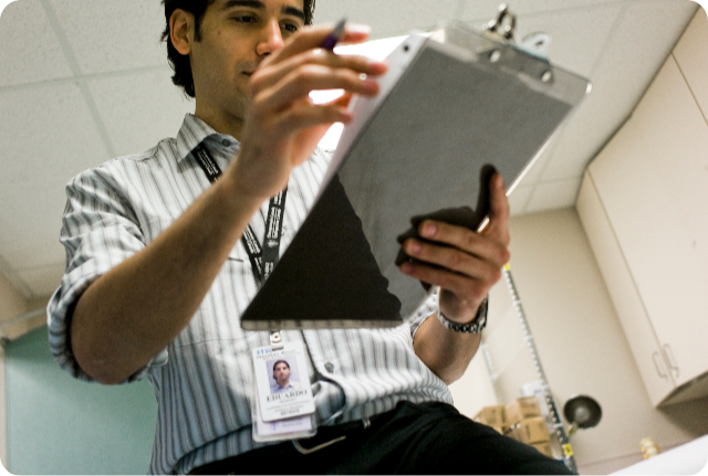 Nurse in an exam room reviewing documents on a clipboard