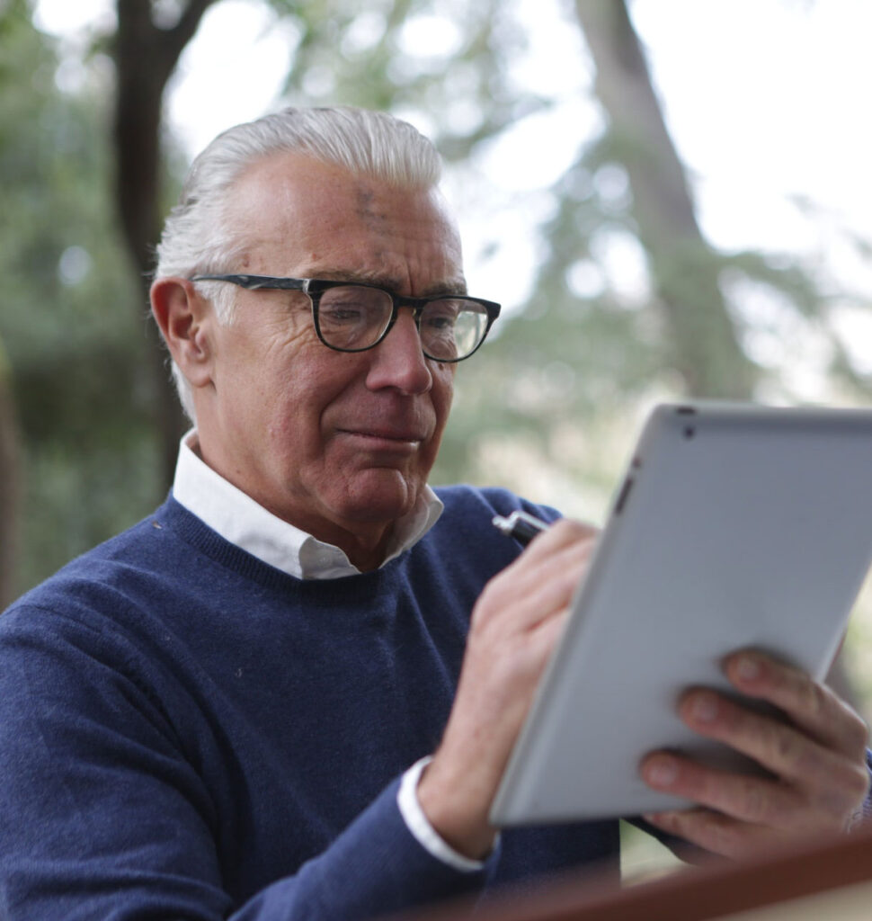 Portrait shot of an elderly man wearing glasses, looking at educational resources on a computer tablet